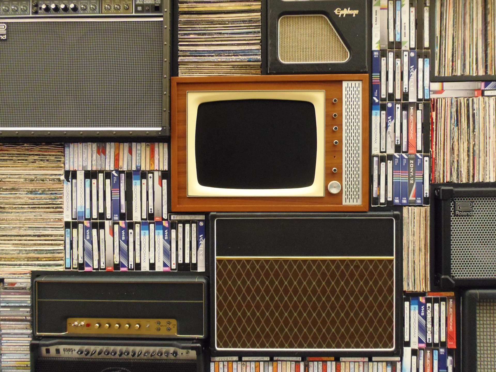Una pared formada por una tele antigua, radios antiguas, cintas y discos.